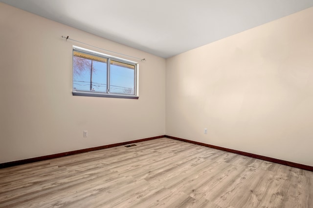 empty room featuring light wood-type flooring, visible vents, and baseboards