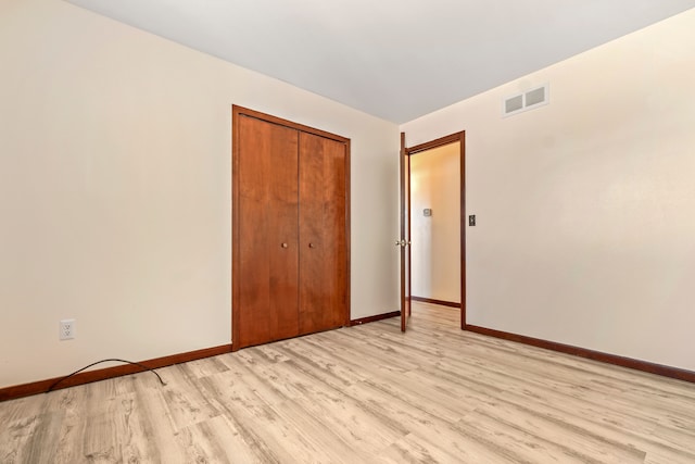 unfurnished bedroom featuring light wood-type flooring, a closet, visible vents, and baseboards