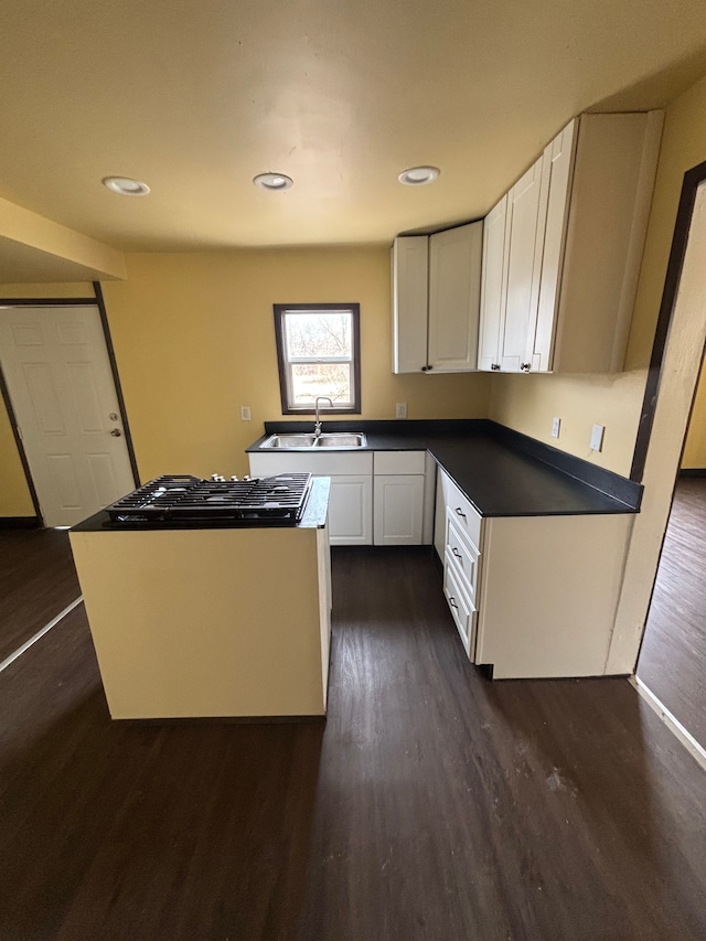 kitchen with dark wood finished floors, dark countertops, a sink, and white cabinetry