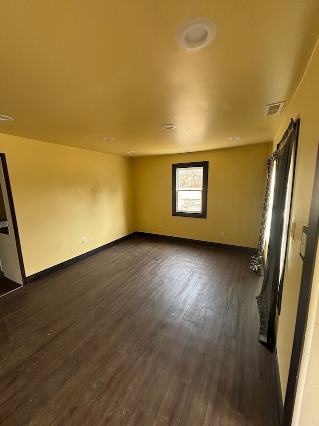 spare room featuring dark wood-type flooring, visible vents, and baseboards