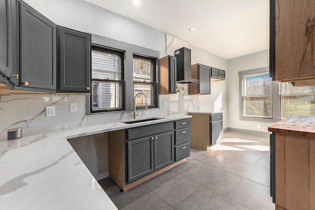 kitchen featuring light tile patterned flooring, a sink, light stone countertops, wall chimney exhaust hood, and tasteful backsplash