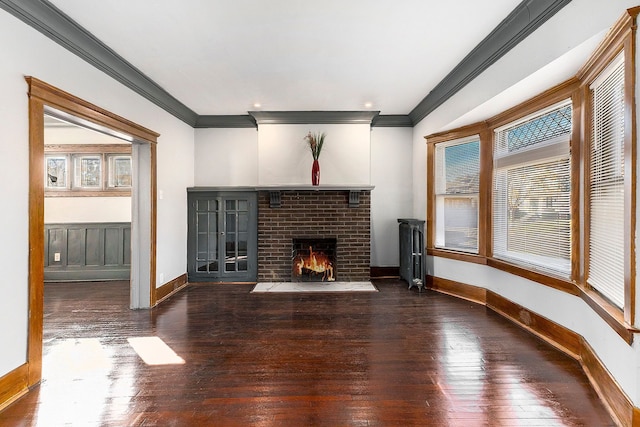 unfurnished living room featuring a brick fireplace, baseboards, ornamental molding, and hardwood / wood-style floors