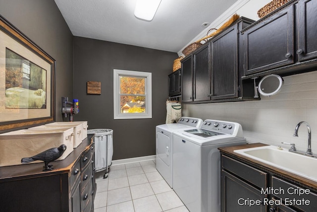 washroom with washing machine and clothes dryer, light tile patterned floors, cabinet space, a sink, and baseboards