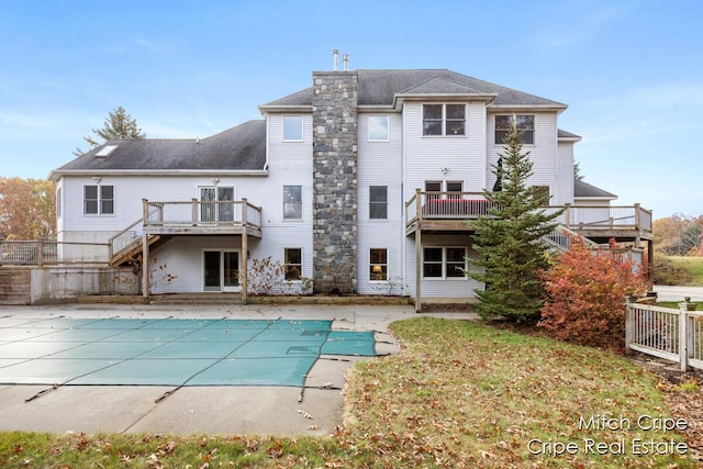 back of property with a covered pool, a patio, a wooden deck, and stairs