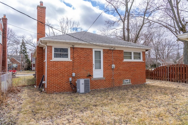 back of property featuring brick siding, a chimney, cooling unit, and fence