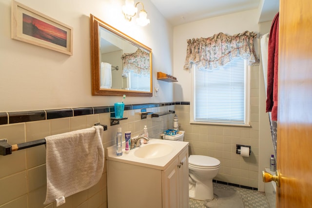 full bath with toilet, a wainscoted wall, tile patterned flooring, vanity, and tile walls