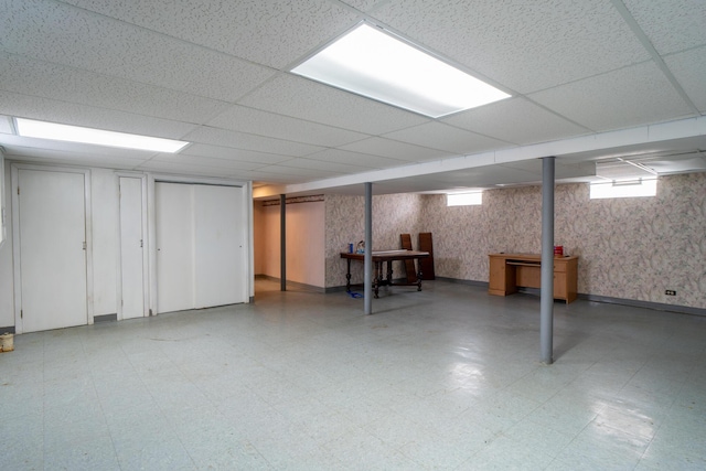 below grade area featuring baseboards, light floors, a drop ceiling, and wallpapered walls