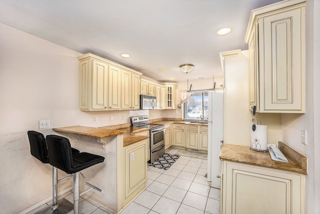 kitchen with a peninsula, appliances with stainless steel finishes, cream cabinets, and a kitchen breakfast bar