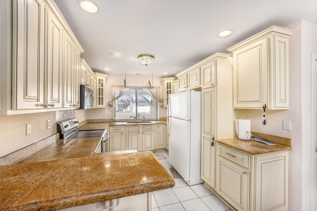 kitchen featuring freestanding refrigerator, cream cabinets, stainless steel electric stove, black microwave, and a sink