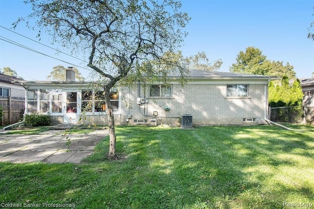 rear view of house with brick siding, fence, a chimney, and a lawn