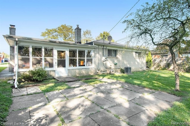 back of house with a lawn, a sunroom, a chimney, cooling unit, and brick siding