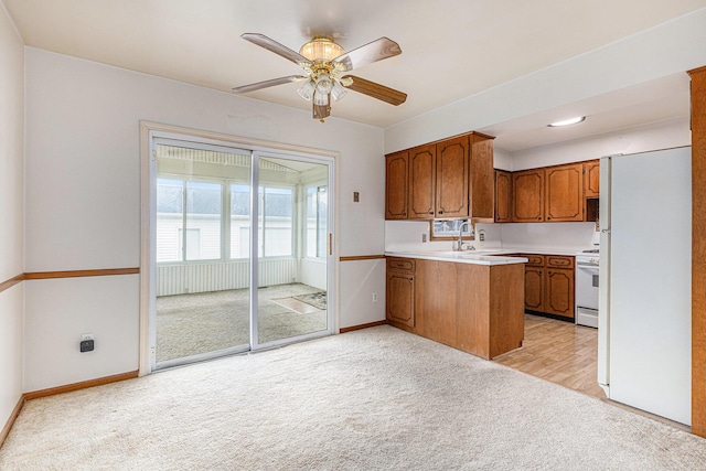 kitchen featuring light carpet, a peninsula, white appliances, and brown cabinets