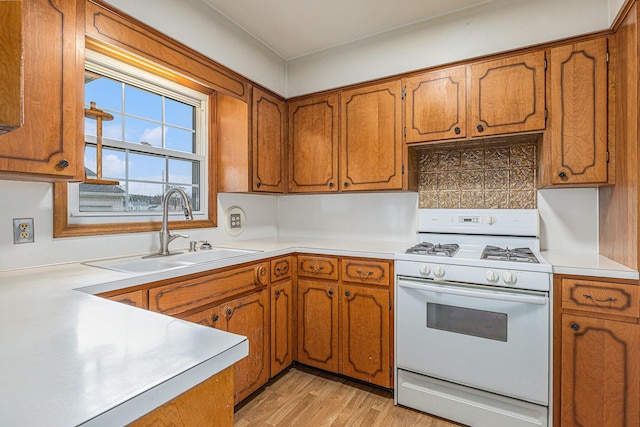 kitchen featuring light countertops, brown cabinetry, a sink, and white range with gas stovetop