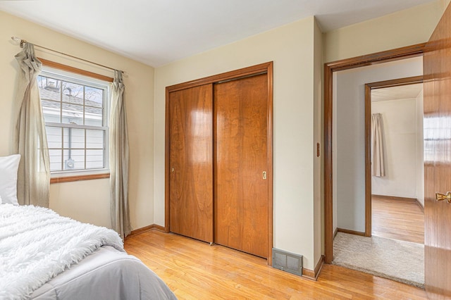 bedroom with baseboards, light wood-style flooring, visible vents, and a closet