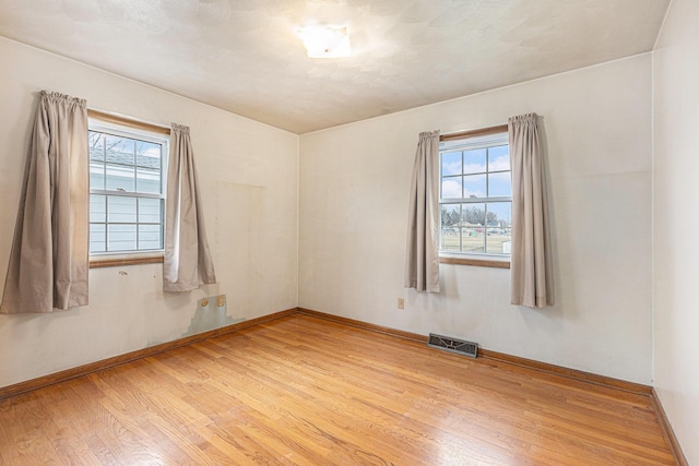 unfurnished room featuring visible vents, light wood-style flooring, and baseboards