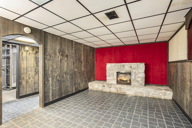 interior space featuring arched walkways, a drop ceiling, wooden walls, a fireplace, and visible vents