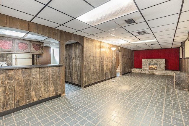 interior space featuring a paneled ceiling, a stone fireplace, wood walls, and visible vents