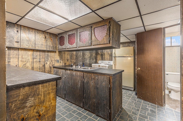 kitchen featuring dark countertops, white appliances, a drop ceiling, and a sink