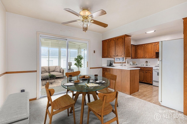 kitchen with brown cabinets, light countertops, a sink, white appliances, and a peninsula