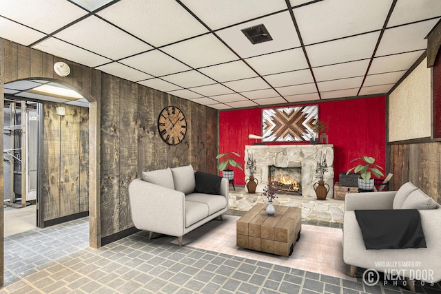 living area with wood walls, visible vents, arched walkways, and a stone fireplace