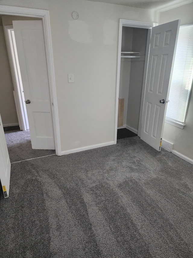 unfurnished bedroom featuring dark colored carpet, a closet, and baseboards