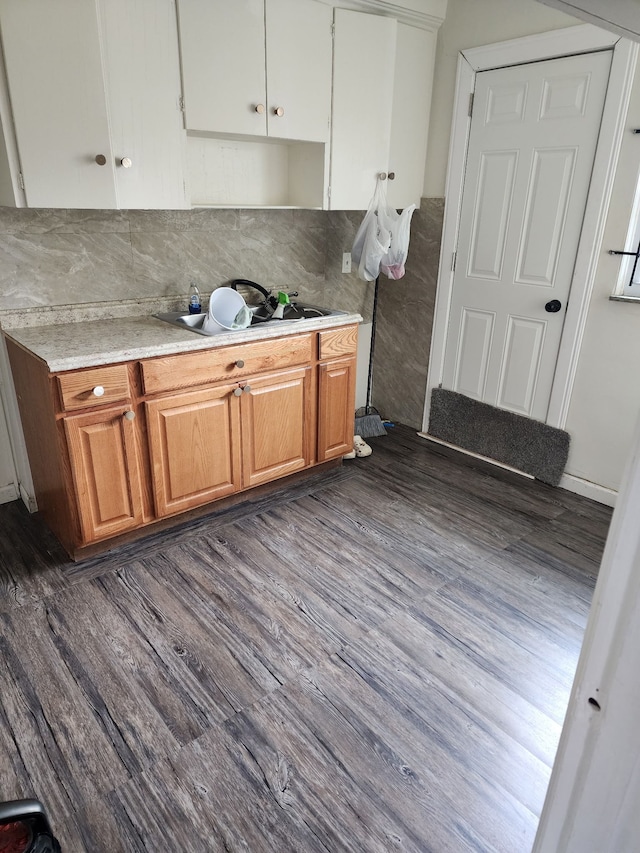 kitchen featuring dark wood-style flooring, a sink, light countertops, backsplash, and brown cabinetry