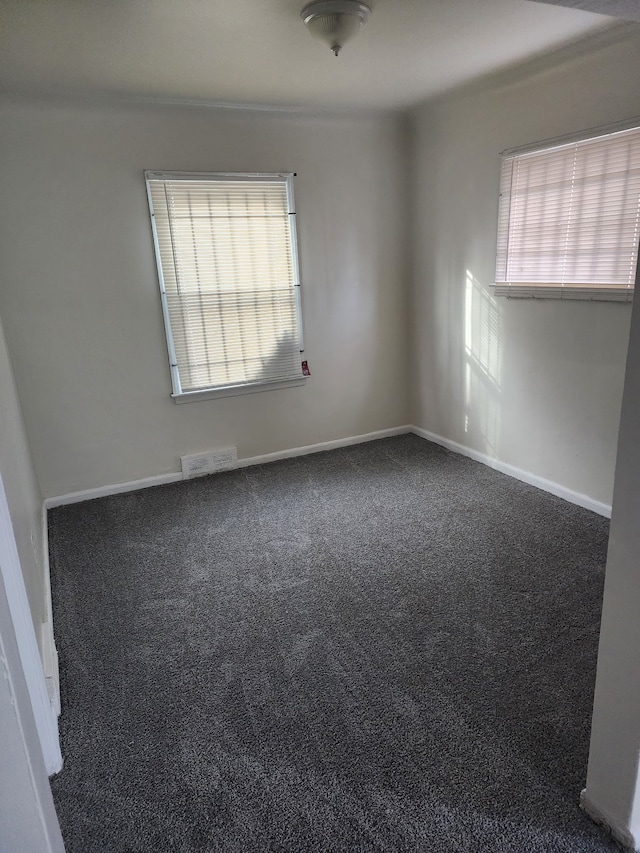 empty room featuring visible vents, dark carpet, and baseboards