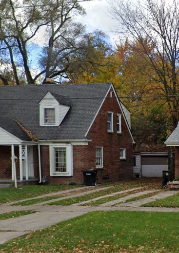 view of side of property with brick siding, roof with shingles, a lawn, a garage, and an outdoor structure