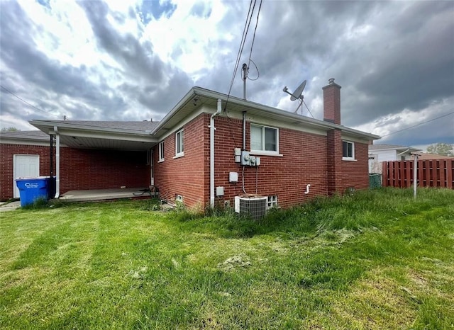 rear view of property featuring a chimney, fence, a lawn, and brick siding