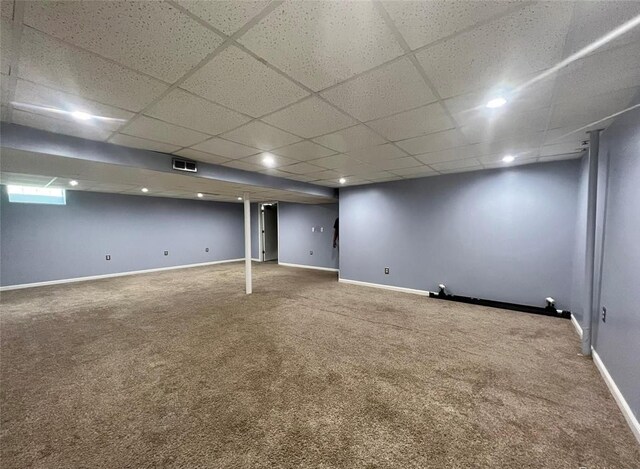 finished basement with carpet, visible vents, a paneled ceiling, and baseboards