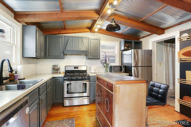 kitchen with appliances with stainless steel finishes, vaulted ceiling with beams, gray cabinets, light wood-style floors, and a sink