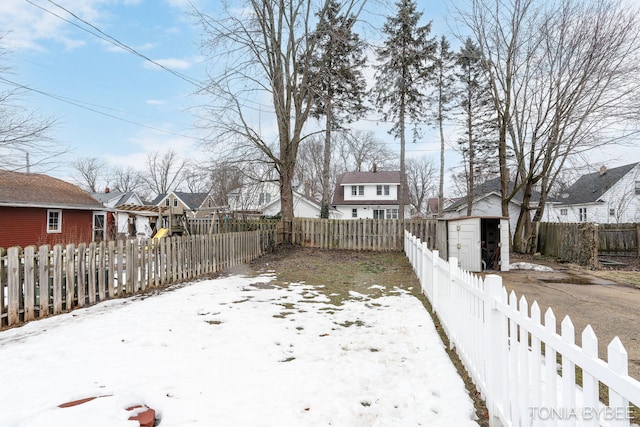 snowy yard with a storage shed, an outdoor structure, a fenced backyard, and a residential view