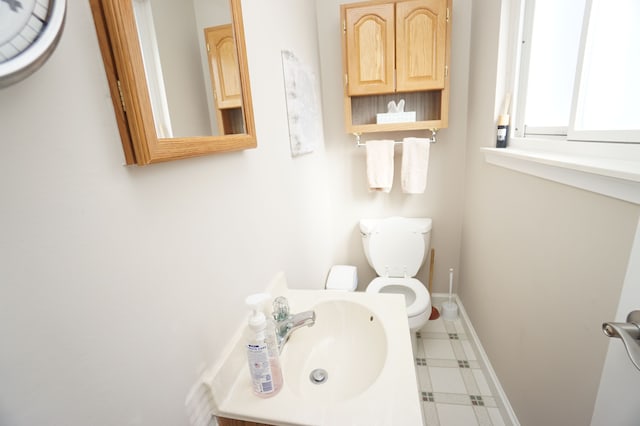 half bath with toilet, baseboards, and a sink