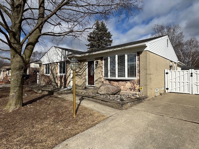 single story home with stone siding, brick siding, concrete driveway, and a gate