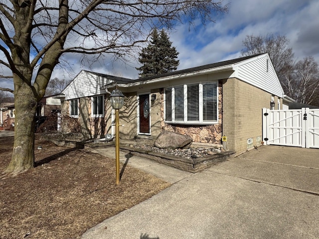 ranch-style house featuring stone siding, a gate, and brick siding