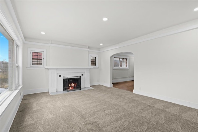 unfurnished living room featuring a fireplace with flush hearth, carpet, plenty of natural light, and arched walkways