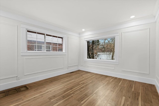 spare room with a healthy amount of sunlight, a decorative wall, visible vents, and wood finished floors