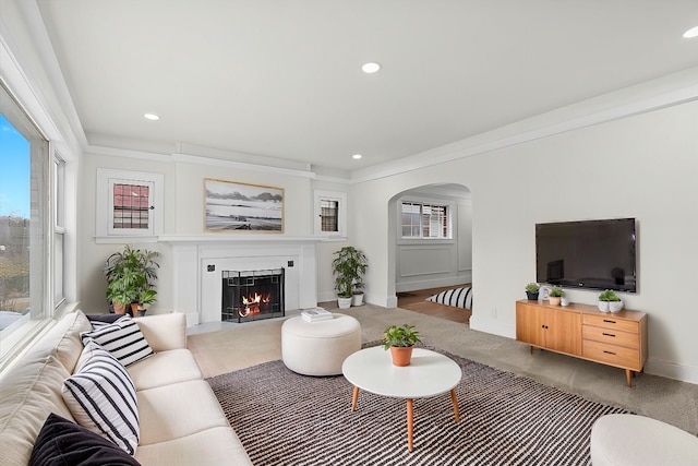 living room featuring arched walkways, a warm lit fireplace, recessed lighting, carpet flooring, and baseboards