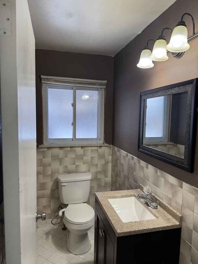 half bath featuring tile patterned flooring, toilet, a wainscoted wall, vanity, and tile walls