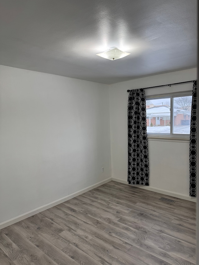 spare room with visible vents, a textured ceiling, baseboards, and wood finished floors