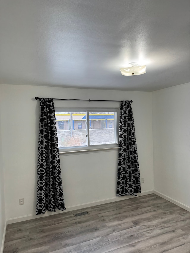 unfurnished room with wood finished floors, visible vents, and baseboards