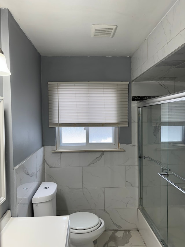 full bath with toilet, an enclosed shower, visible vents, and tile walls