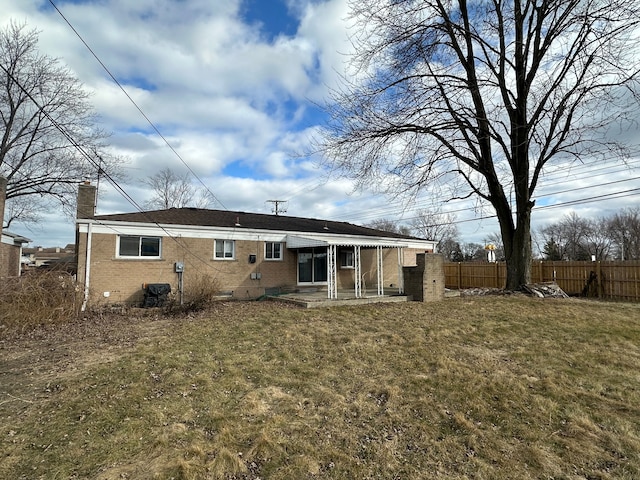 rear view of property featuring a yard, brick siding, fence, and a chimney