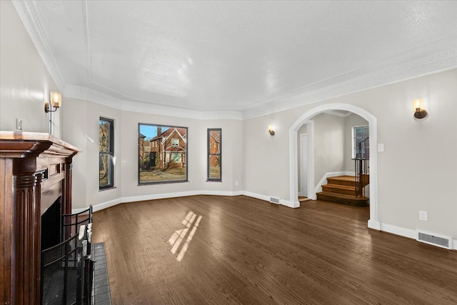 unfurnished living room with visible vents, a brick fireplace, baseboards, arched walkways, and dark wood-style flooring