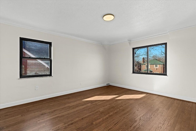 spare room featuring crown molding, wood finished floors, baseboards, and a textured ceiling