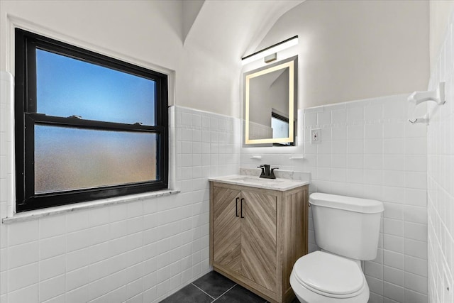 bathroom with tile patterned flooring, tile walls, a wainscoted wall, toilet, and vanity