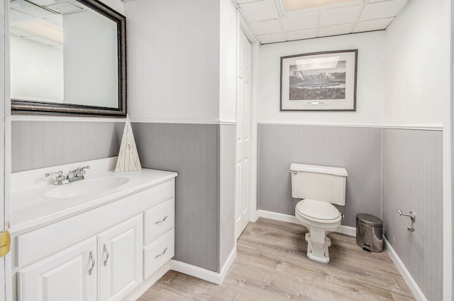 bathroom featuring toilet, a drop ceiling, wood finished floors, and wainscoting