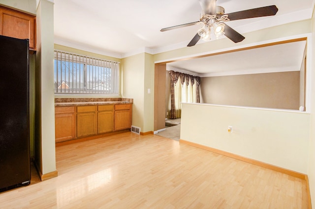 kitchen with light wood-style flooring, visible vents, freestanding refrigerator, brown cabinets, and crown molding