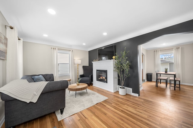 living room with recessed lighting, baseboards, a glass covered fireplace, and light wood finished floors