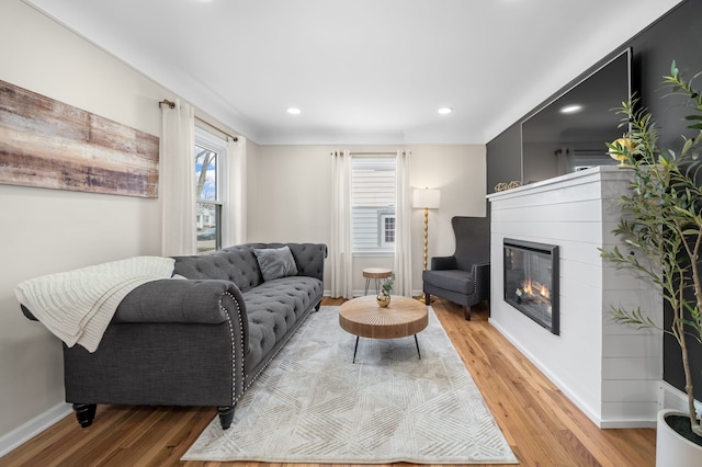 living area with a glass covered fireplace, recessed lighting, light wood-type flooring, and baseboards